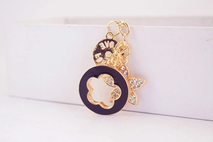 Detailed close-up of golden clover keychain with black enamel camellia and rhinestones