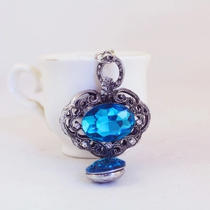 Pendentif vintage en argent avec cristal bleu ovale et strass blancs sur une tasse blanche