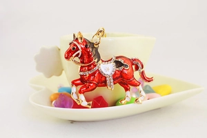 Dettaglio macro di portachiavi cavallo in smalto rosso con strass su tazza decorativa