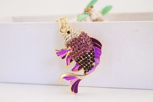 Detailansicht eines fischförmigen Schlüsselanhängers mit lila Strass und Emaille