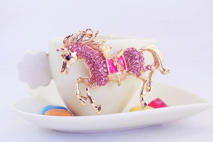 Detailed macro view of gold flying horse pendant with pink rhinestones and enamel saddle