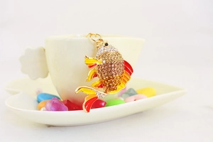 Detailansicht Goldfisch-Schlüsselanhänger mit Strasssteinen und Emaille-Flossen an einer Tasse