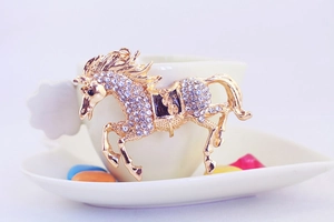 Detail of a sparkling golden horse keychain with white rhinestones on a ceramic cup