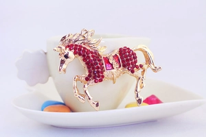 Detailed close-up of a golden horse keychain charm with red rhinestones on a coffee cup