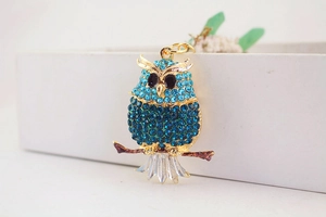 Close-up of golden owl keychain with blue rhinestones standing on a brown branch