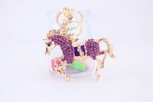 Close-up of golden flying horse keychain with purple rhinestones and blue saddle detail