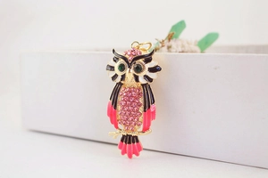 Detailopname van een gouden uil sleutelhanger met roze strass-steentjes en groene ogen
