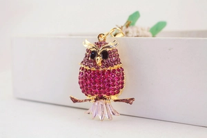 Close-up of owl keychain with purple rhinestones on golden branch and white gift box