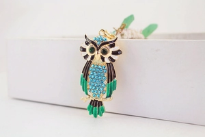 Detail van uil-sleutelhanger met blauwe strass-steentjes en groene edelsteenogen