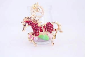 Detail shot of a golden flying horse keychain featuring sparkling red rhinestones