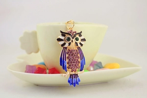 Detail van de gouden uil sleutelhanger met paarse strass en blauwe emaille lak
