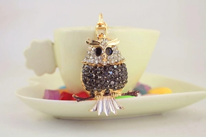 Detailed view of the rhinestone owl keychain hanging on a light yellow coffee cup saucer