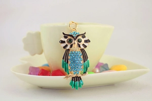 Detail van uil sleutelhanger met blauwe kristallen en groene ogen aan een koffiekop