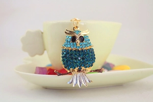 Detail of cute rhinestone owl keychain with blue crystals hanging on a ceramic cup
