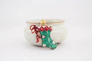 Macro detail of green enamel Christmas stocking brooch with red bow and sparkling zircons