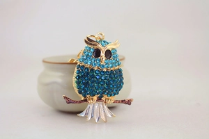Detailed close-up of a golden owl keychain with sparkling blue rhinestones on a branch