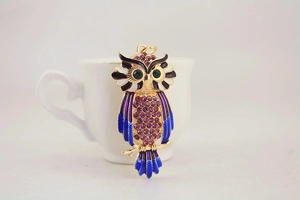 Detail of owl keychain featuring purple rhinestones and blue enamel on a white cup