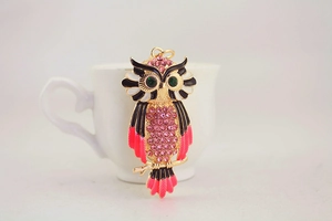 Detail of pink rhinestone owl keychain with emerald green eyes on a white ceramic cup