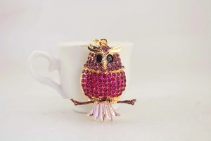 Close-up of owl keychain with purple rhinestones on a golden branch and white cup
