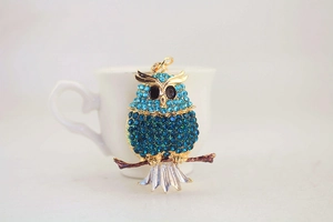 Detailed view of owl keychain with blue crystals and gold base on a branch