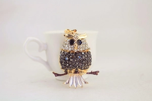 Close-up of rhinestone owl keychain with crystals on branch next to a ceramic cup