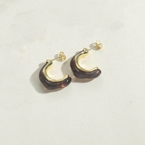 Detalle de pendientes de resina en forma de C con marco dorado y diseño de carey