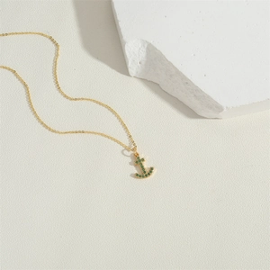 Collana con ancora placcata in oro con ciondolo in zircone verde su sfondo bianco