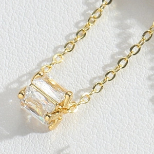 Detailed macro view of a gold-toned necklace featuring a claw-set rectangular zircon stone