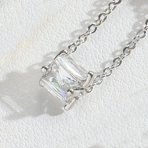 Macro shot of a silver square zircon pendant on a delicate link chain over white leather