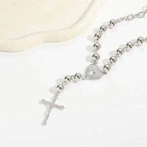 Collier argenté avec pendentif cœur et croix sur chaîne à billes exposé sur plateau