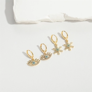 Detail of gold huggie earrings with evil eye and starburst charms featuring white zircons