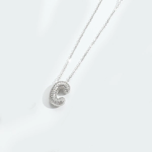 Macro shot of silver letter C pendant with micro-paved crystals on a delicate chain