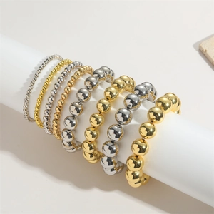 Detail van gestapelde gouden en zilveren kralenarmbanden op een witte displaystand