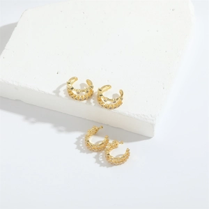 Detailed macro view of minimalist gold double-row ear cuffs and pave-set C-shape earrings