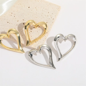 Exaggerated hollow heart earrings in polished gold and silver on stone and silk background