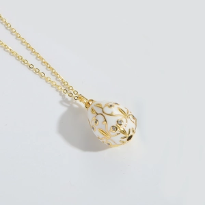 Close-up of white enamel egg pendant with gold vine patterns and sparkling crystals