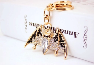Close-up of golden bat keychain with black and clear rhinestones on a white book