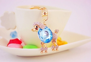 Dettaglio portachiavi a barboncino con gemma blu e finitura oro su una tazza di caffè