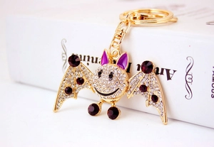 Detailed close-up of gold bat keychain with purple crystals and pavé setting on a white book