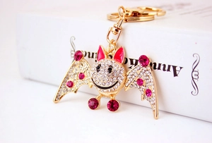 Close-up of golden bat keychain with sparkling white and pink crystals and red enamel ears
