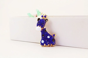 Détail macro du pendentif girafe doré avec strass bleus et finitions en émail chic