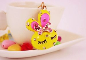 Detail of yellow rabbit keychain with pink crystals and enamel finish on white background
