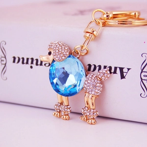 Portachiavi barboncino dorato con gemma blu e strass bianchi su scatola decorativa