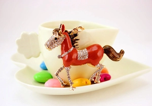 Detail of red enamel horse keychain with sparkling rhinestones on a coffee cup