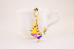 Détail macro du porte-clés oiseau jaune en émail coloré posé sur une tasse blanche