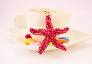 Close-up of golden starfish keychain with sparkling pink rhinestones on white cup