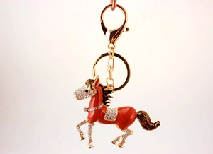 Close-up of golden horse keychain with orange enamel and sparkling white crystal inlay