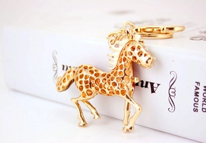 Detail of a golden metal horse keychain with cutout design leaning against a white book
