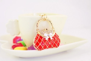 Detail of red enamel handbag keychain with gold trim and white bow on porcelain