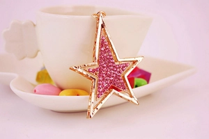 Détail macro d'un porte-clés étoile dorée serti de strass roses posé sur une tasse à café